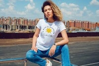 a woman sitting on a railing wearing a white t - shirt with a sun on it