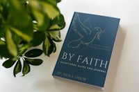 the book by faith is sitting on a table next to a plant