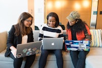 three women sitting on a couch with laptops